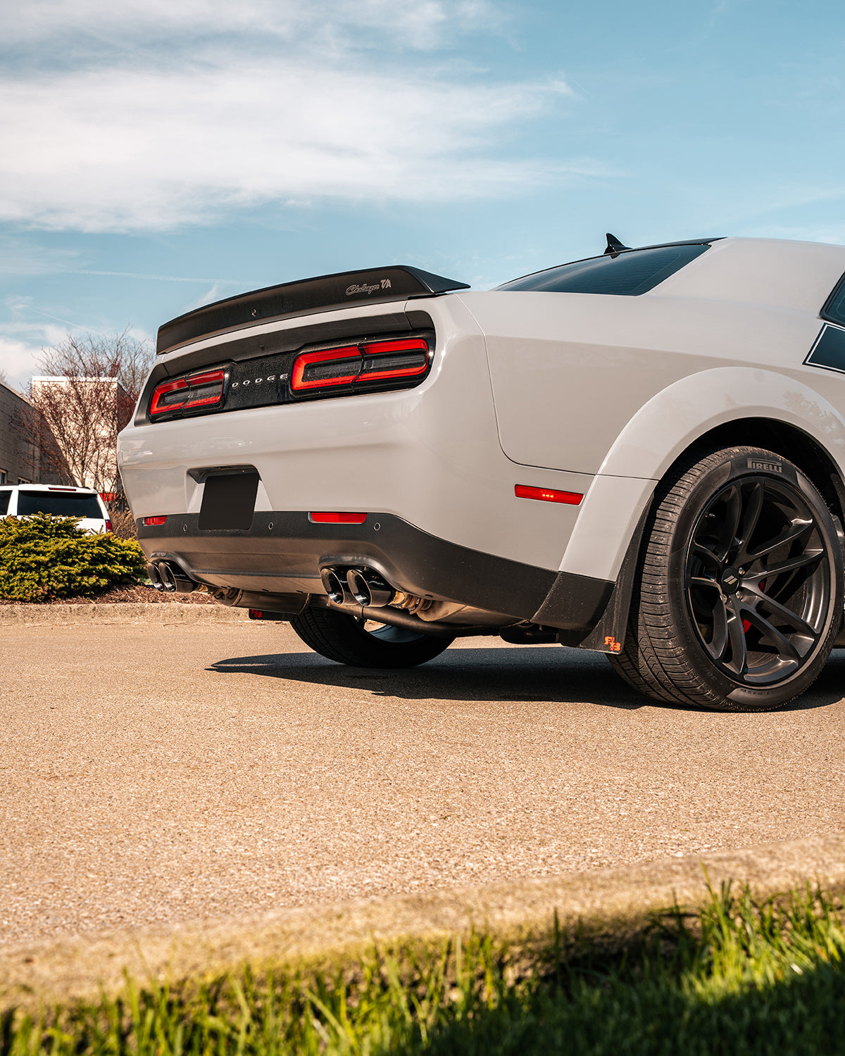 White widebody Dodge Challenger seen from the rear quarter with quad exhaust tips and a rear spoiler
